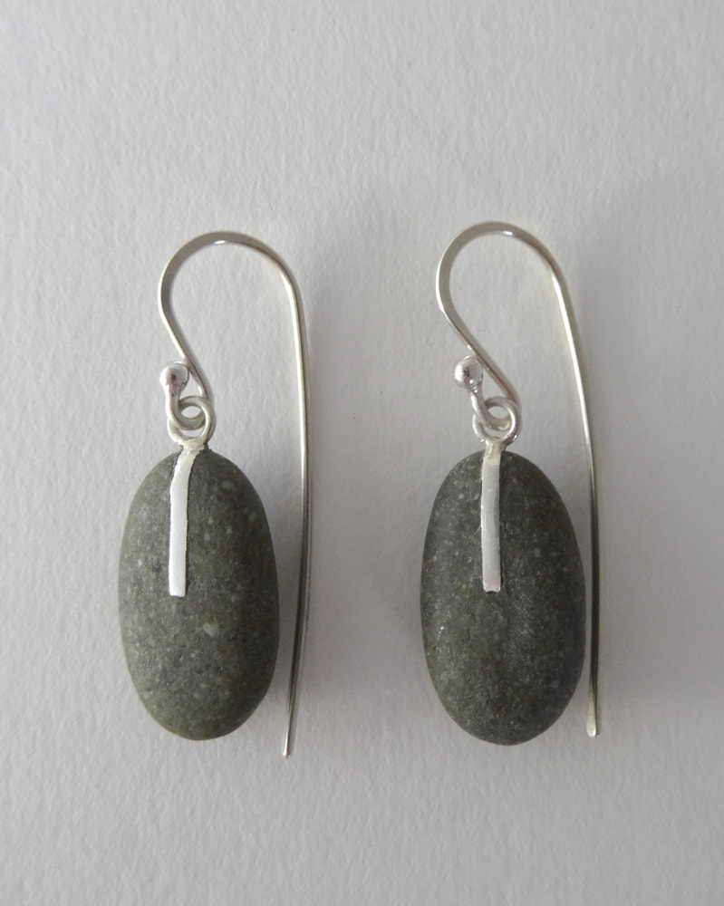 These Earrings are made from Sterling Silver and Greywacke Pebbles. Maike collected the pebbles on Birdlings Flat beach on the South Island of New Zealand. A straight Silver line was inlayed into the stone.